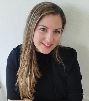 Dr Villegas Plá has long blonde hair. She is wearing a black top and blazer, looking upwards slightly at the camera and smiling. 